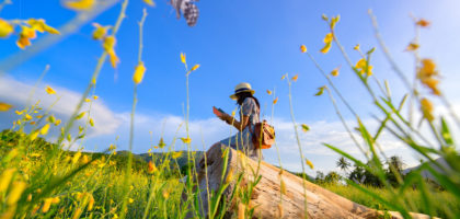 Woman enjoying reading a book on a timber log in the middle of a field of wildflowers